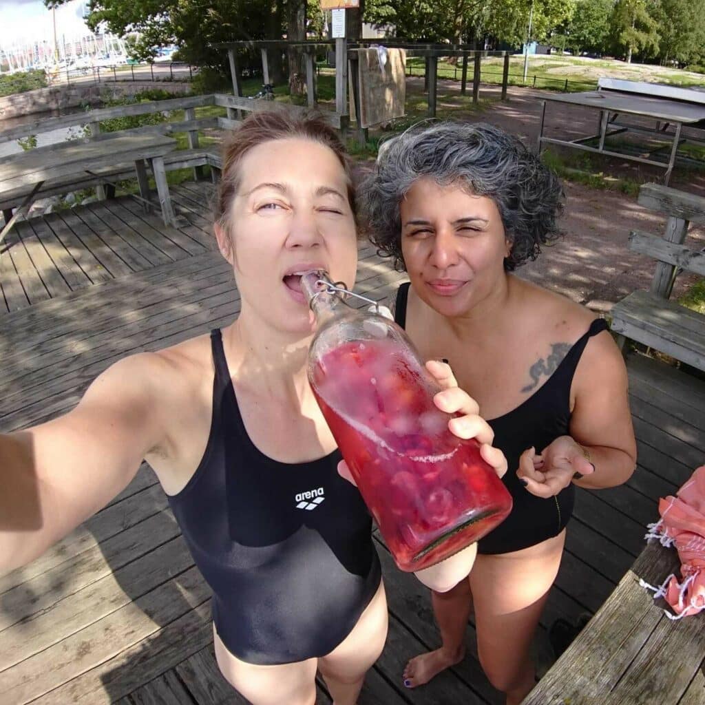 two people in swimsuits looking at the camera, one of them drinking from a glass bottle